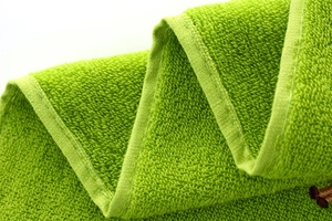 Close-up of vibrant green cotton towel showing soft looped texture and durable edge stitching