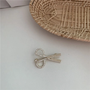 Detailed close-up of a scissor-shaped gold brooch with elegant pearls and sparkling rhinestones
