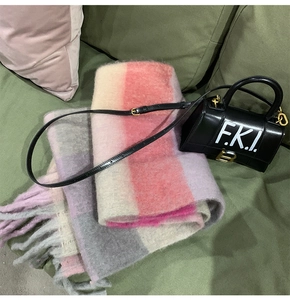 Plaid tassel scarf in pink, gray, and beige draped next to a black top-handle leather bag