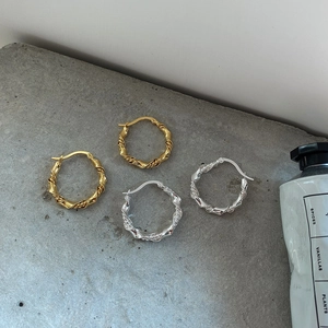 Macro detail of twisted braided hoop earrings in polished gold and silver finish