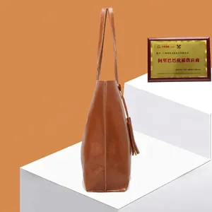 Minimalist brown oil wax leather bucket bag with tassel charm on a display stand