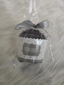 Cupcake-shaped grey fuzzy wine socks with ribbon bow packaging on white plush surface