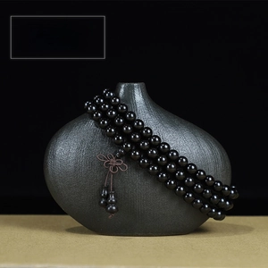 Close-up of 108 ebony wood prayer beads with gourd pendant on a ceramic vase