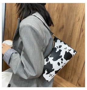 Detail of a black and white cow print baguette shoulder bag worn over a grey blazer