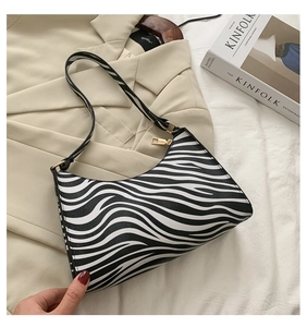 Detail of zebra pattern shoulder bag with gold zipper on beige blazer and magazine