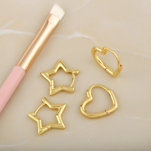 Golden minimalist star and heart earring set on marble surface with makeup brush