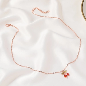 Macro shot of cherry pendant with red crystals and green leaves on rose gold chain