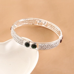 Macro detail of silver bangle with multicolored crystals on white ceramic heart tray