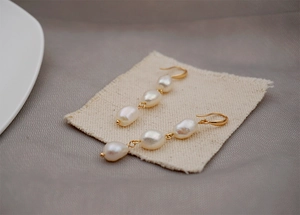 Close-up of triple Baroque freshwater pearl drop earrings on a linen background