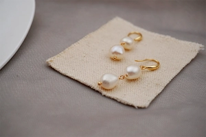 Close-up of golden drop earrings with white baroque pearls on rustic linen fabric