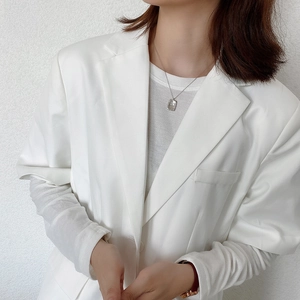 Detail shot of a square hammered silver pendant necklace worn by a model in white blazer