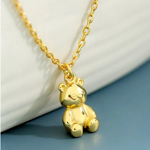 Macro shot of a golden teddy bear pendant with polished finish on a minimalist fine chain