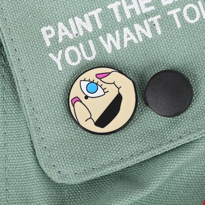 Artistic Picasso style enamel eye brooch pinned on green denim fabric background