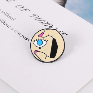 Artistic round enamel pin featuring Picasso-style eye and hand design on card