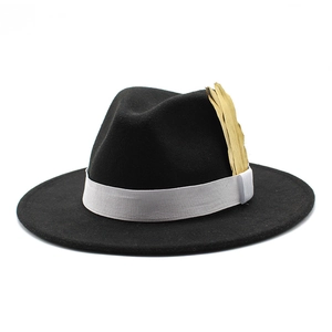 Detail of a black wool felt fedora featuring a white grosgrain ribbon and golden feather