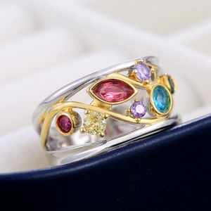 Macro shot of colorful gemstone ring with gold floral vine detail on a blue jewelry box