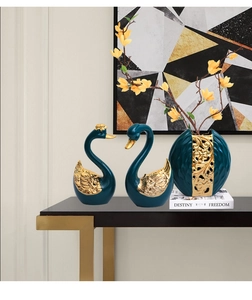 Detail of luxury ceramic swan ornaments and vase with gold accents on a black console table