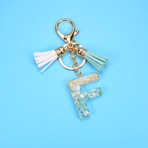 Detail of resin letter F keychain with gold foil, blue stones and colorful tassels