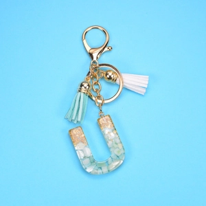 Detailed macro view of letter U resin keychain with gold foil, stones and blue tassels