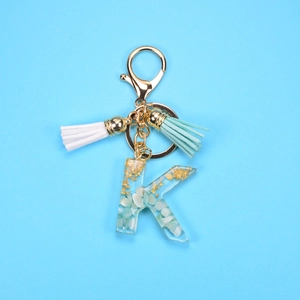 Detailed macro view of resin letter K keychain with gold flakes and mint green tassels