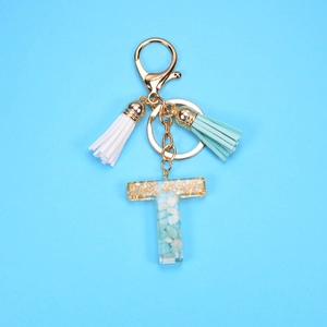 Detail of letter T keychain with light blue stones, gold flakes, and tassels on blue base