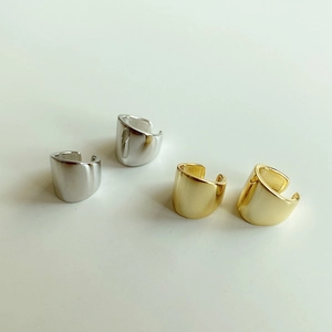 Polished silver and gold wide-band ear cuffs displayed on a clean beige background