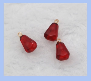 Close-up of translucent burgundy resin pomegranate seed charms with golden rings