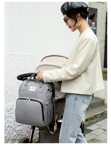 Grey multi-functional diaper backpack hanging on a stroller in a bright outdoor setting