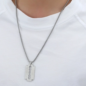Detail of silver razor blade pendant on a box chain worn on a white shirt