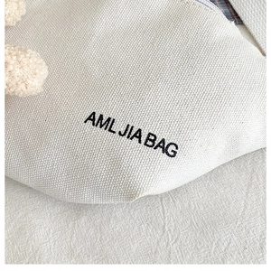 Detail of off-white canvas crossbody bag with AML JIA BAG print and durable stitching