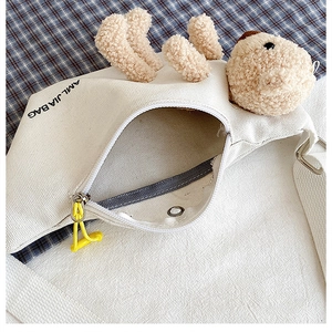 Detailed view of cream canvas crossbody bag with plush bear motif and yellow zipper pull