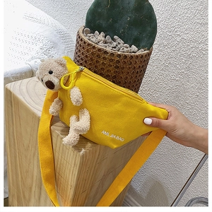 Yellow canvas crossbody bag with a 3D plush bear on a light wood base