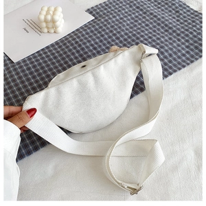 Close-up of a white canvas chest bag with adjustable strap and metal zipper on fabric
