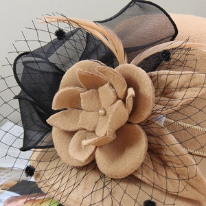 Détail d'une fleur élégante en feutre de laine camel avec voile en résille noire et plumes
