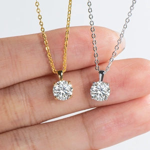 Close-up of gold and silver moissanite necklaces held by hand to show pendant size