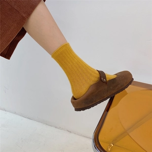 Detail of mustard yellow ribbed wool sock paired with brown suede mule on orange chair