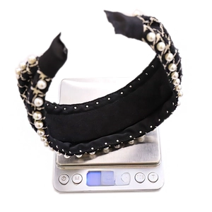 Detailed top view of a wide black fabric headband with pearls and gold chains on a scale