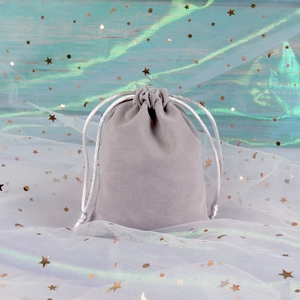 Close-up of light grey velvet drawstring jewelry pouch on decorative blue background