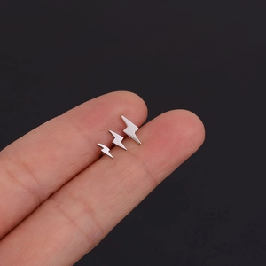 Set of three mini stainless steel lightning bolt stud earrings on a fingertip