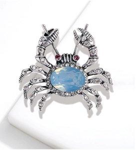Macro shot of silver crab brooch with blue gemstone and white rhinestones on white base