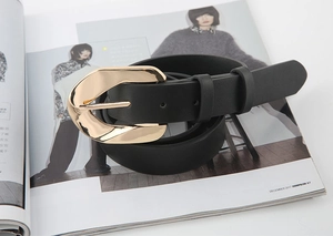 Detail of a black leather belt with a golden buckle styled on a fashion magazine
