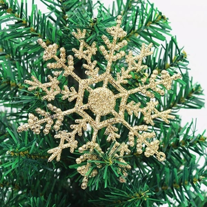 Sparkling gold glitter snowflake ornament hanging on a lush green Christmas tree branch