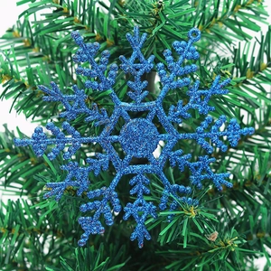 Sparkling light blue snowflake ornament with glitter finish hanging on a green Xmas tree