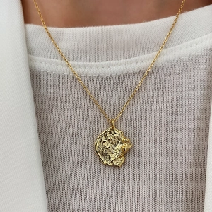 Golden 925 silver necklace with irregular embossed pendant on white knitwear background
