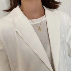 Detail of a minimalist gold necklace with a round irregular embossed coin pendant on a model