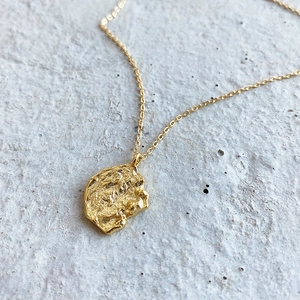 Macro shot of gold irregular textured circular pendant necklace on grey stone background