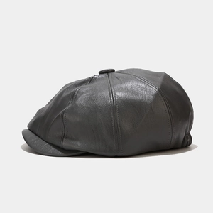 Detail view of dark grey leather newsboy cap showing texture and stitching on white background