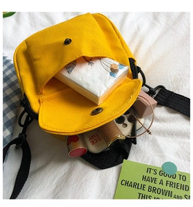 Detail view of yellow canvas crossbody bag with multi-layer zipper storage and daily items