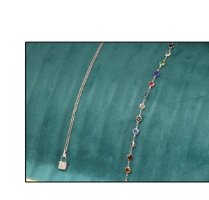 Detail of silver necklace with padlock pendant and colorful gemstone bracelet on dark green velvet