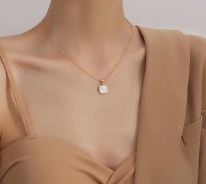 Detail of a gold stainless steel necklace with a square white mother of pearl pendant
